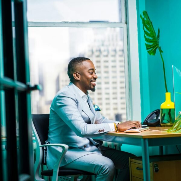 Confident businessman in modern office working on laptop with city view.