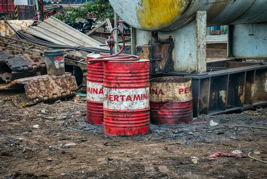 Rusted Pertamina oil barrels in an industrial waste area outdoors in Jakarta, Indonesia.