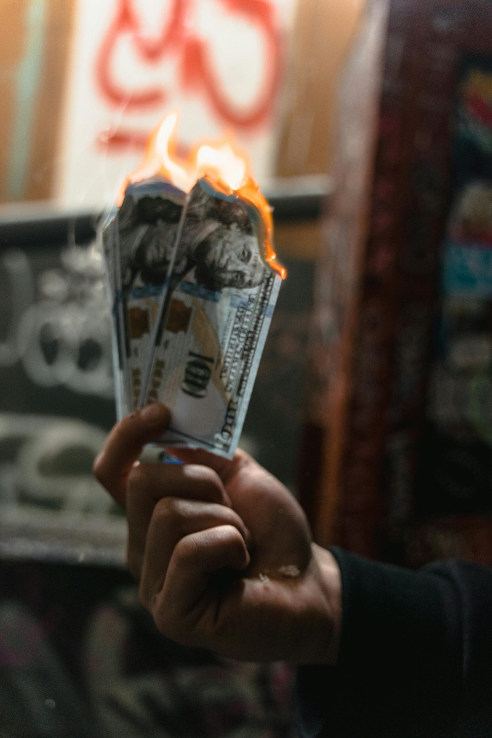 Dramatic image of burning dollar bills held against a graffiti-covered wall, symbolizing waste.